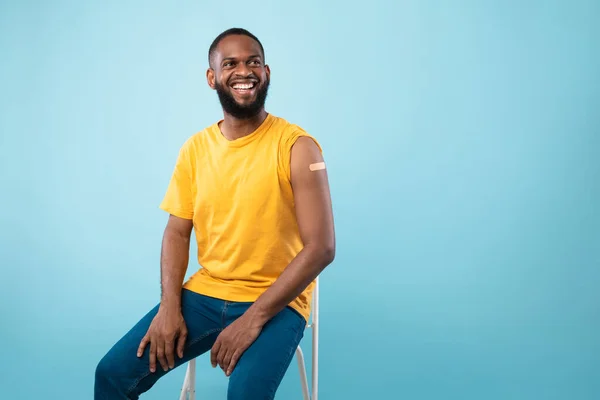 Vaccinerad svart kille visar axeln med band stöd gips efter anti covid vaccin skott på blå studio bakgrund — Stockfoto