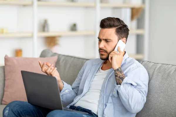 불만에 찬 밀레니엄 남자가 전화로 이야기하고 노트북을 보고 인터넷 연결, 복사 공간에 문제가 있습니다. — 스톡 사진