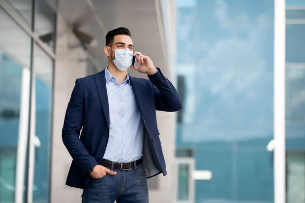 Empreendedor do Oriente Médio em máscara facial falando ao ar livre por telefone — Fotografia de Stock