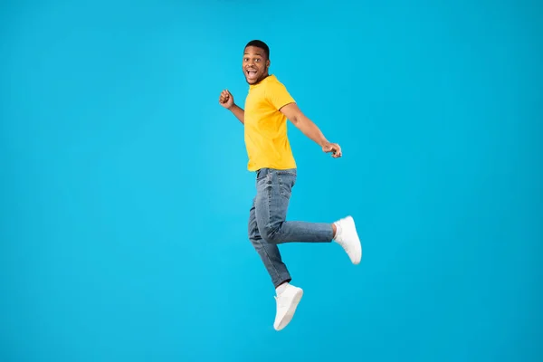 Despreocupado afro-americano homem saltando sorrindo para a câmera, fundo azul — Fotografia de Stock