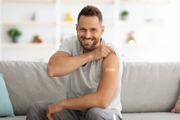 Gelukkige jonge gevaccineerde man met schouder met medisch gips na vaccinatie en brede glimlach voor de camera — Stockfoto