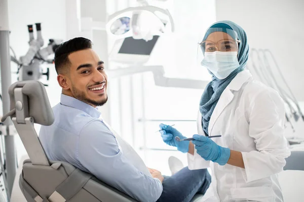 Porträt einer glücklichen islamischen Stomatologin, die sich bei einem männlichen Patienten untersuchen lässt — Stockfoto