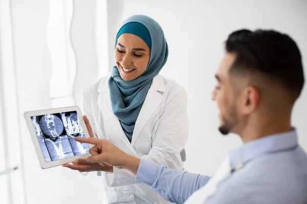 Mujer dentista islámica mostrando los dientes de rayos X en la tableta digital para el paciente masculino —  Fotos de Stock