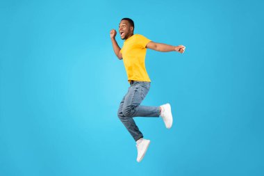 Orta havada zıplayan ve bağıran neşeli Afrikalı adam, mavi arka plan