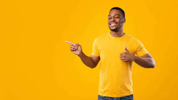 African American Guy Pointing Finger Aside Gesturing Thumbs-Up, Yellow Background — стокове фото