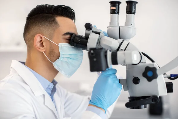 Trabalhador médico masculino árabe usando microscópio, fazendo pesquisa no laboratório moderno — Fotografia de Stock