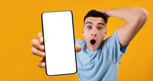 Шокированный мужчина показывает белый пустой экран смартфона рядом с камерой — стоковое фото