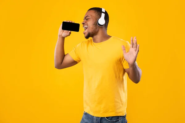 Noir homme chantant tenant Smartphone comme microphone sur fond jaune — Photo