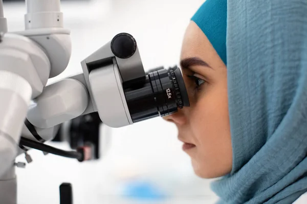 Vista lateral do médico dentista islâmico feminino no Hijab usando microscópio dentário — Fotografia de Stock