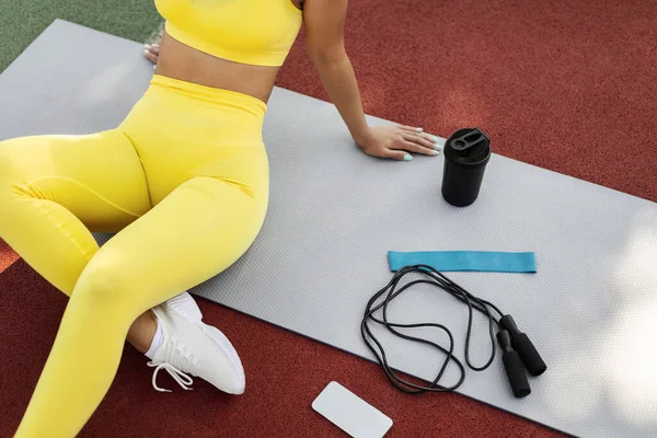 Donna nera in abbigliamento sportivo giallo seduta su tappetino con attrezzatura — Foto Stock