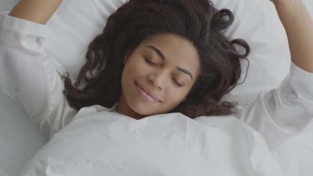 Ovanifrån porträtt av ung välsovande afrikansk amerikansk kvinna sträcker sig i sängen och ler mot kameran — Stockvideo