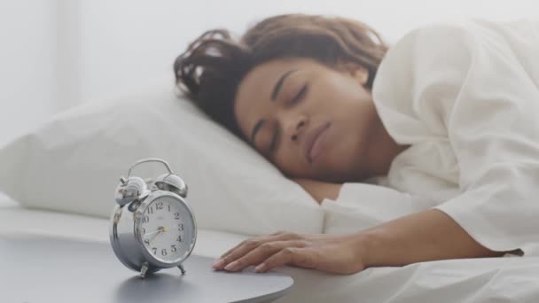 アフリカ系アメリカ人の若い女性が目覚まし時計を鳴らしベッドで寝て — ストック動画