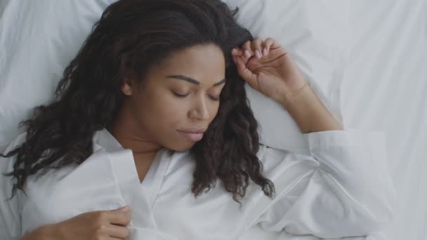 Ovanifrån porträtt av ung afrikansk amerikansk kvinna sover i sängen, bär vit negligé, vilar hemma på morgonen — Stockvideo