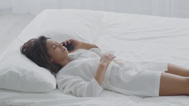アフリカ系アメリカ人の若い女性が激しい腹痛に苦しみ、ベッドに横になって痛みを求めて医者に電話する — ストック動画