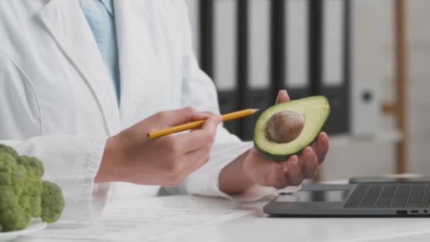 Nutrición alternativa. Primer plano inyección de médico nutricionista irreconocible explicando los beneficios del aguacate — Vídeo de stock