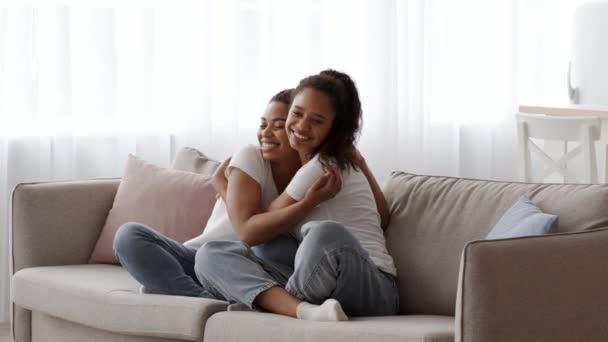 Twee gelukkige Afro-Amerikaanse zusters knuffelen elkaar op bank thuis — Stockvideo
