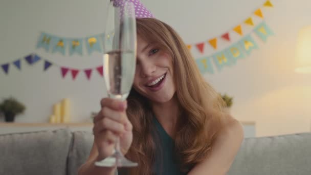 Webcam pov portrait of cheerful woman in party cap blowing up whistle and cheering with champagne glass to camera — Stock Video