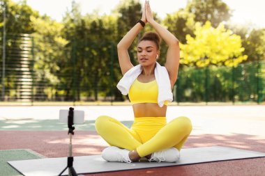 Genç bir kadın akıllı telefonun önünde oturmuş meditasyon yapıyor.