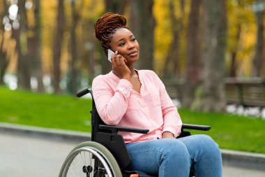 Tekerlekli sandalyedeki genç Afro bayan sonbaharda şehir parkında telefon görüşmesi yapıyor.