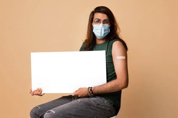 Middle-eastern young man in mask got vaccinated, holding blank board — Stock Photo, Image
