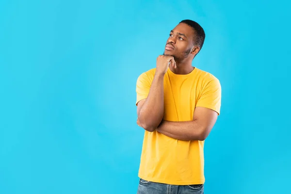 Afro-Amerikaanse man denkend aangrijpende kin kijken opzij, blauwe achtergrond — Stockfoto