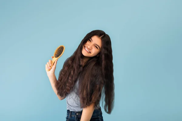 Attraente ragazza adolescente indiana con lunghi capelli scuri setosi in possesso di spazzola di legno, posa su sfondo blu studio — Foto Stock