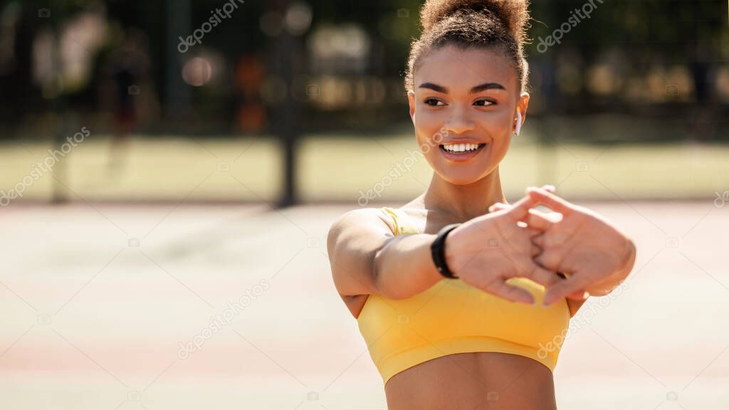 Sporty black woman in yellow sportswear stretching arms