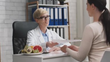Neşeli kadın beslenme uzmanı ofisteki mutlu kadın hastaya beslenme planı veriyor, minnettar bayan doktorların elini sıkıyor.