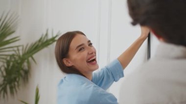 Yeni dairenin duvarına resim asarken kocasına gülen genç pozitif kadının yakın portresi.