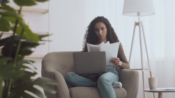 Junge irritierte Frau arbeitet mit Dokumenten, wirft Papiere und blickt verzweifelt auf Laptop — Stockvideo