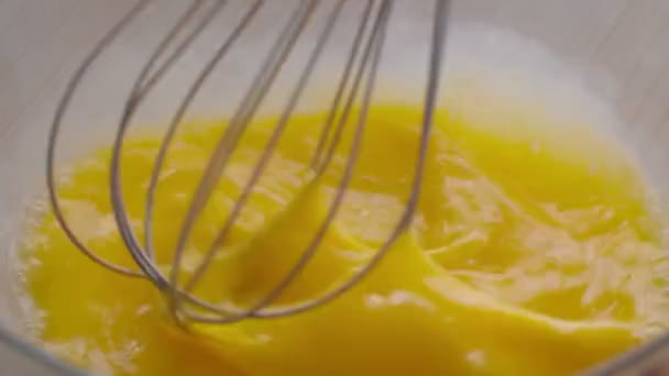 Готовлю яичницу. Крупный план шеф-повара, смешивающего яичный желток с металлическим венчиком в миске, готовящего тесто на кухне — стоковое видео