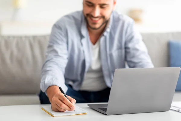 Mannelijke freelancer schrijven in notitieblok en met behulp van laptop, met behulp van computer, het noteren van informatie van internet, selectieve focus — Stockfoto
