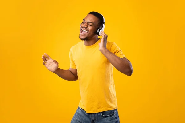 Negro chico cantando usando auriculares y bailando sobre amarillo fondo — Foto de Stock