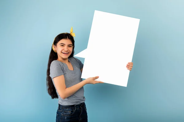 Wesoły indyjski nastolatek dziewczyna trzyma puste mowy bańki, oferując miejsce na reklamę na niebieskim tle studio, makieta — Zdjęcie stockowe