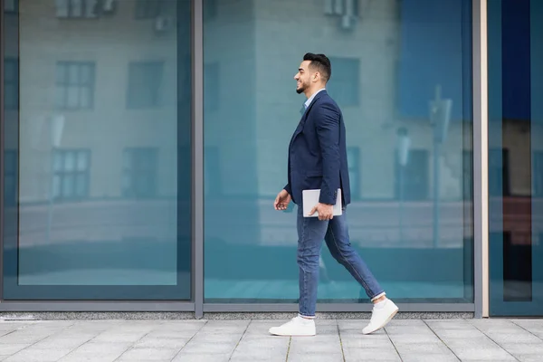 Hombre de negocios árabe alegre con almohadilla caminando por la calle, longitud completa — Foto de Stock