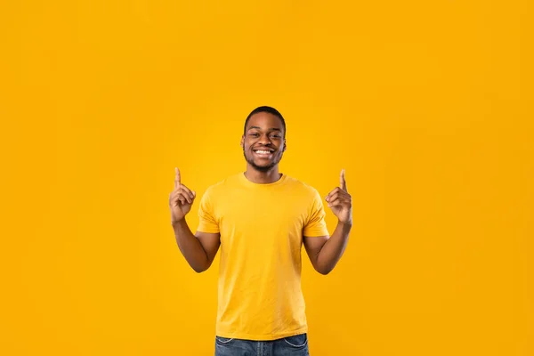 Szczęśliwy czarny człowiek wskazując palce w górę pokazując coś, żółty tło — Zdjęcie stockowe