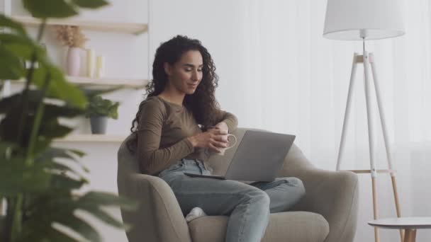 디지털 TV 컨셉. 편안 한 젊은 숙녀가 온라인에서 영화를 보고, 안락 의자에 앉아 노트북 과 차 한잔을 집에서 — 비디오