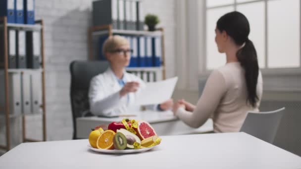 Programm zur Gewichtsreduktion. Verschwommene professionelle Ernährungsberaterin berät Patientin und gibt Diätplan im Büro — Stockvideo