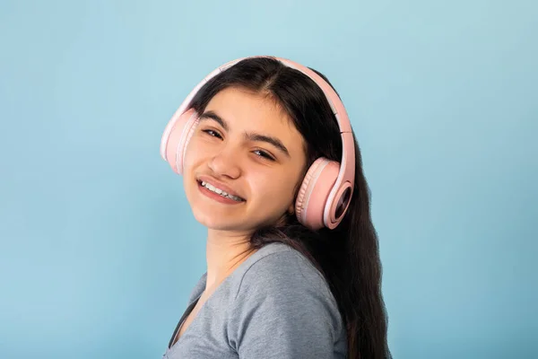 Indiaas tiener meisje in casual dragen luisteren naar muziek in roze draadloze hoofdtelefoon, genieten van cool lied op blauwe achtergrond — Stockfoto