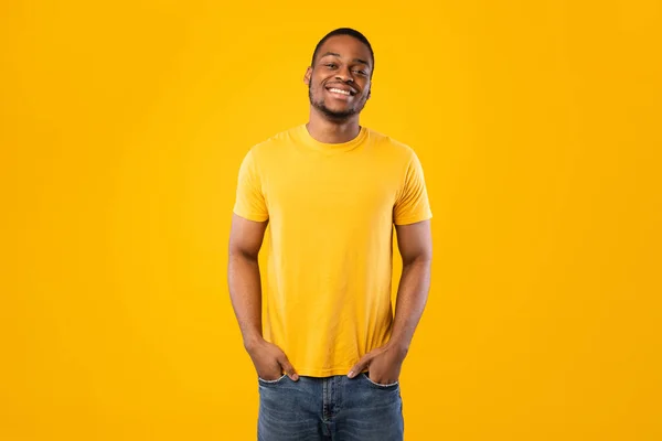 Hombre afroamericano posando con las manos en los bolsillos, fondo amarillo — Foto de Stock