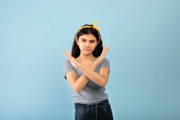 Indiana adolescente gesturing STOP, cruzando as mãos perto do peito no fundo do estúdio azul — Fotografia de Stock