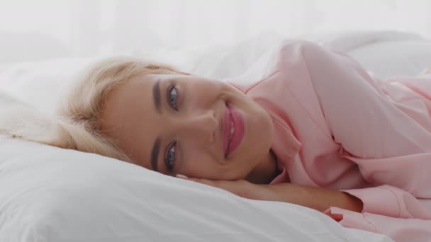 Bonjour. Bonjour. Belle jeune femme blonde se réveillant dans un lit confortable — Video