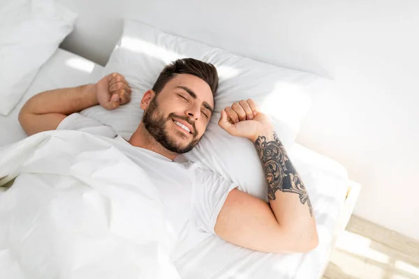 Gelukkig goed geslapen man wakker in de ochtend, stretching terwijl liggend in comfortabel bed en glimlachende, hoge hoek uitzicht — Stockfoto