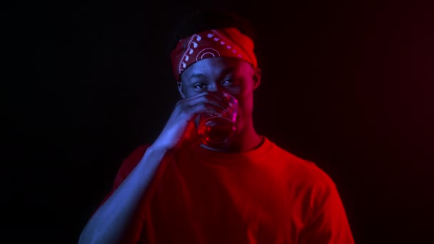 Счастливый афроамериканец тысячелетней давности пьет воду в темной студии — стоковое видео