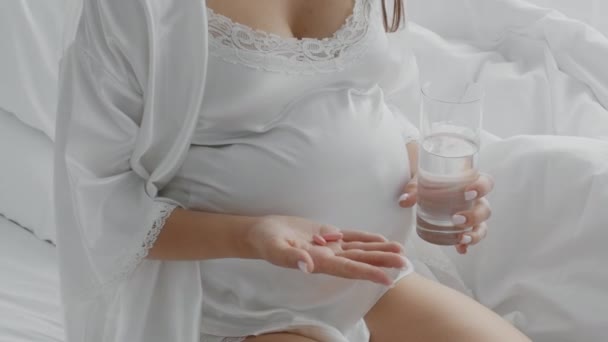 Suplementy przedporodowe. Nierozpoznawalna kobieta w ciąży trzymająca tabletki witaminowe i szklankę wody — Wideo stockowe