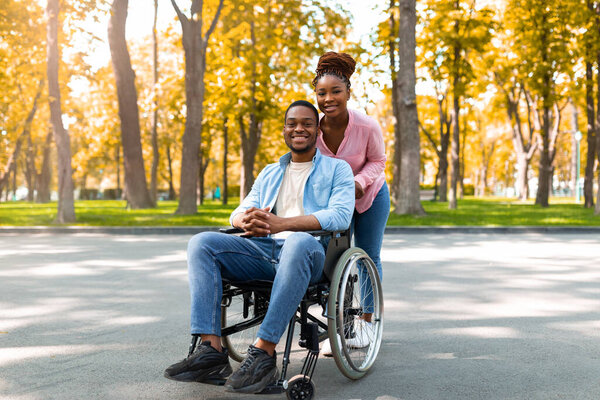 Disabled black man in wheelchair on walk with his loving wife outdoors in autumn, spending fun time together