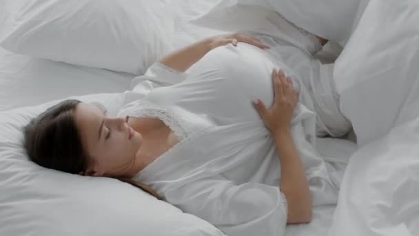 Νεαρή έγκυος γυναίκα με μεγάλη κοιλιά στροφή, ενώ βρίσκεται στο κρεβάτι — Αρχείο Βίντεο