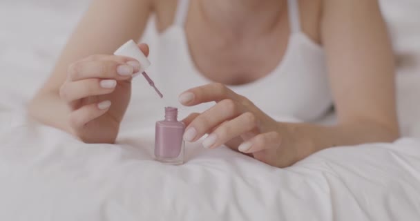 Rilassati. Primo piano colpo di donna irriconoscibile facendo manicure se stessa, applicando smalto sulle unghie, sdraiato a letto — Video Stock
