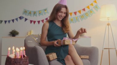 Doğum günü partisi kutlaması. Genç, mutlu bir kadın hediye kutusunu açıyor, dekore edilmiş bir odada koltukta oturuyor.