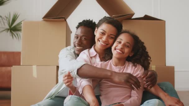 Nuevos propietarios de viviendas. Retrato de la feliz familia afroamericana de tres abrazos sobre cajas de cartón casa — Vídeo de stock